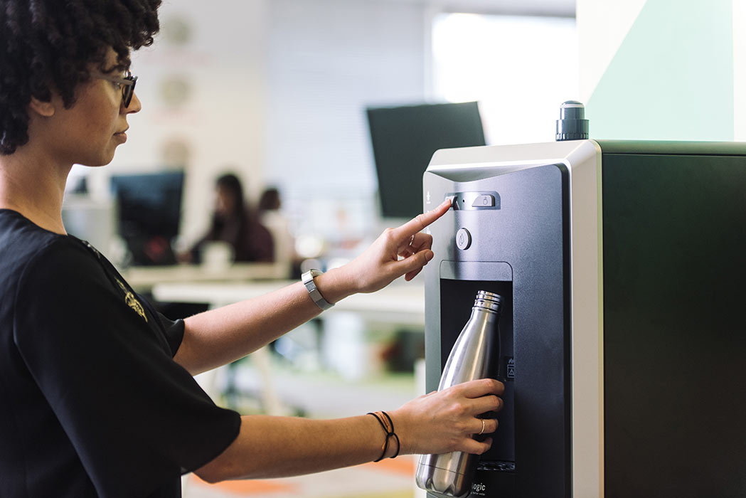 Maquina dispensadora de agua con tecnología para la salud, donde aparece una mujer rellenando una botella